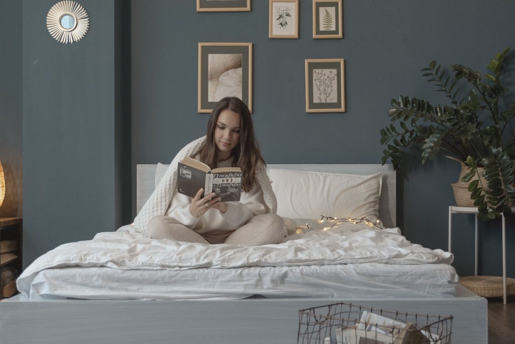 Woman Sitting on Bed while Reading a Book